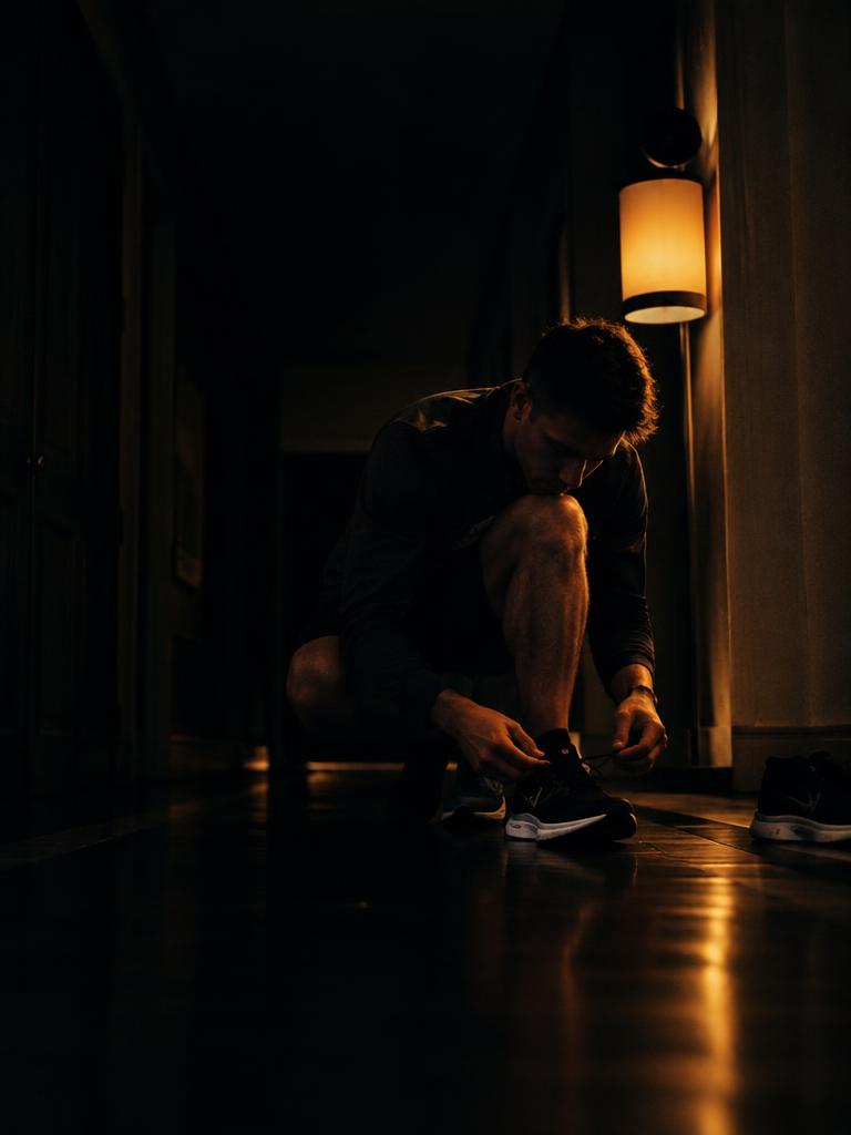 Illustrative image: a man lacing his running shoes in a dark hallway before dawn